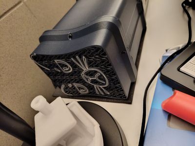 Black cube-shaped mini PC with a patterned side vent, resting on the floor